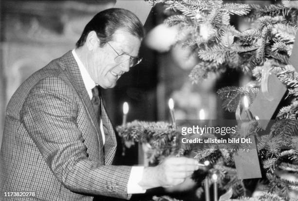Roger Moore lights candles on a Christmas tree