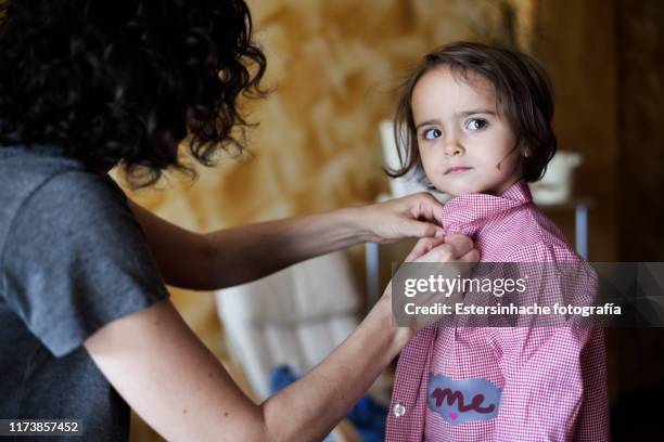 photograph of a family in which the mother is dressing her daughter to go to school, on her first day - vestirse fotografías e imágenes de stock