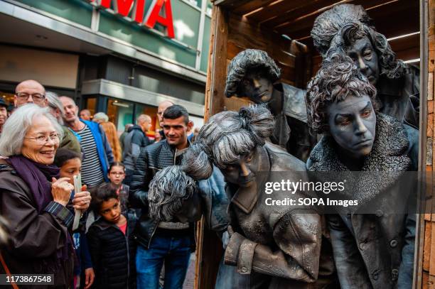 Group of performers are being surrounded by people on the street. The World Living Statues Festival has evolved in thirteen years into the worlds...