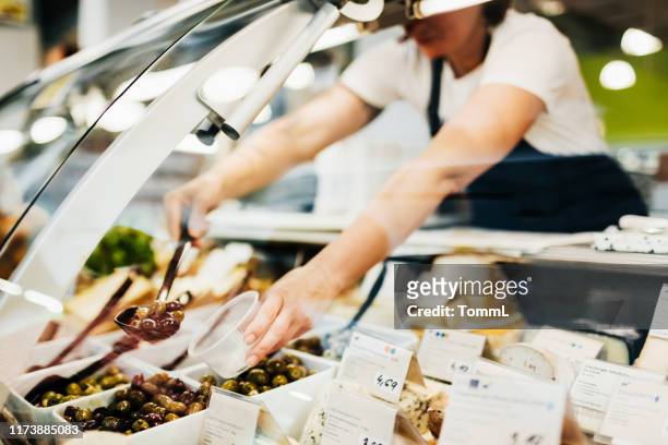 close up of supermarket clerk filling cup with olives - delicatessen stock pictures, royalty-free photos & images