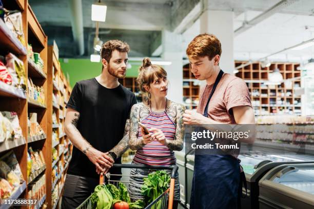 supermarkt bediende assisteren jong stel terwijl boodschappen doen - shop assistant stockfoto's en -beelden