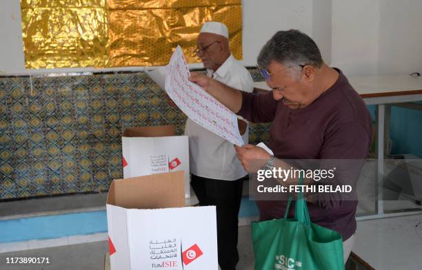 Tunisian men read the list of candidates behind voting booths at a polling station in the capital Tunis on October 6 during the third round of...