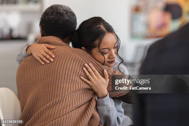supportive women hug while attending a group therapy session - perdão imagens e fotografias de stock