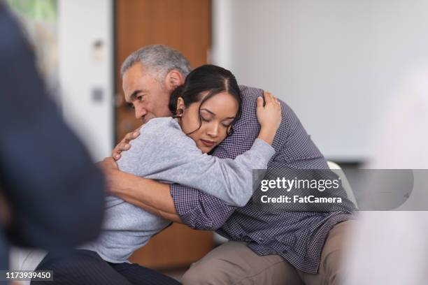 father gives daughter a supportive hug in a group therapy session - victim help stock pictures, royalty-free photos & images