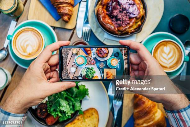 man photographing breakfast in a cafe with smartphone - photographing fotografías e imágenes de stock