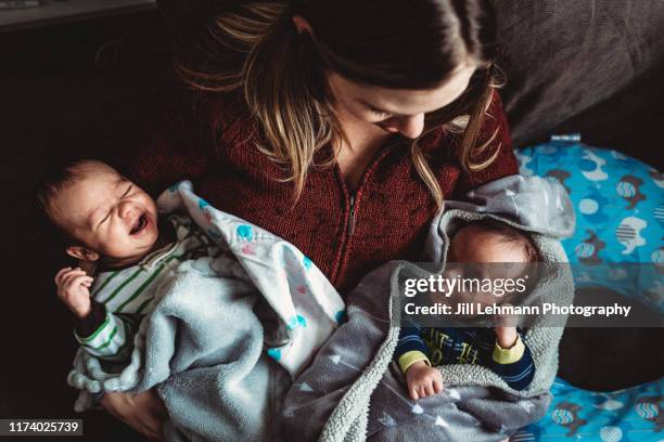 mother holds infant newborn twins together at home on lap - tweeling stockfoto's en -beelden