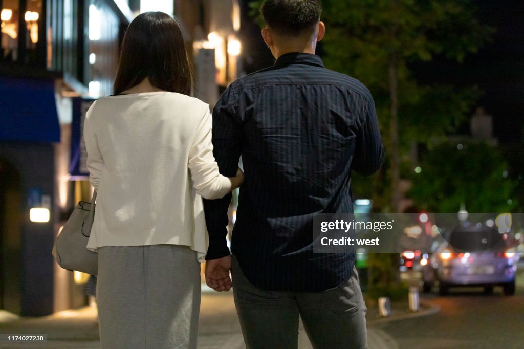 夜間在市中心手牽手行走的男女的後視圖