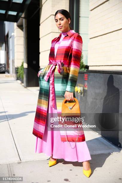 Guest is seen posing with a colorful overcoat and orange purse at Spring Studios during New York Fashion Week on September 11, 2019 in New York City.