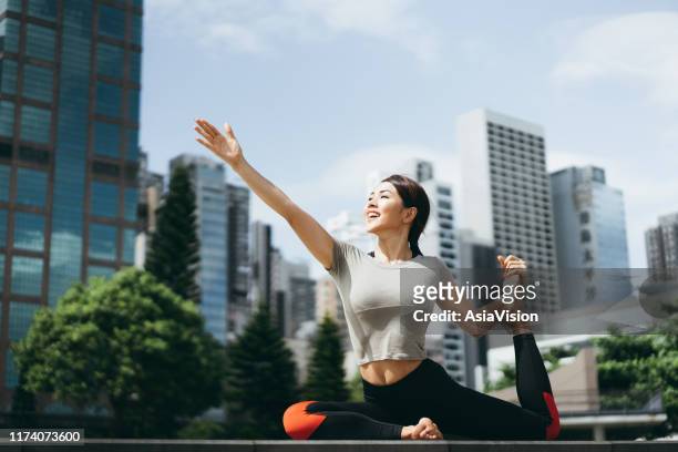 atletische jonge aziatische vrouw beoefenen yoga buitenshuis in stadspark tegen stedelijk stadsgezicht in de ochtend - hongkong lifestyle stockfoto's en -beelden
