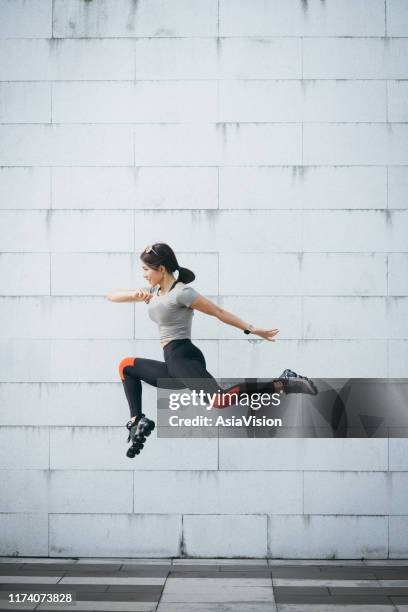 vertrouwen en energieke jonge sportieve vrouw springen in de lucht tegen de grijze muur in het stadspark - wellbeing city stockfoto's en -beelden