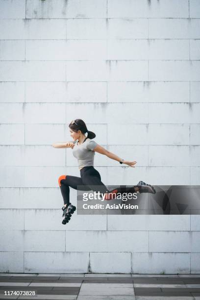 confidence and energetic young sporty woman jumping in air against grey wall at city park - sportswear stock pictures, royalty-free photos & images