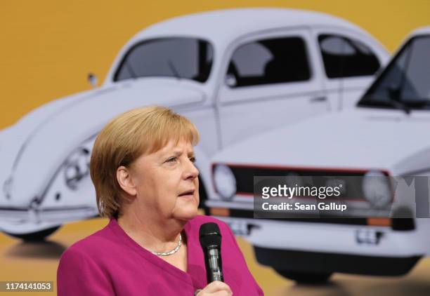 German Chancellor Angela Merkel stands next to images of older Volkswagen cars, including the VW Beetle and Golf, during a tour of stands on the...