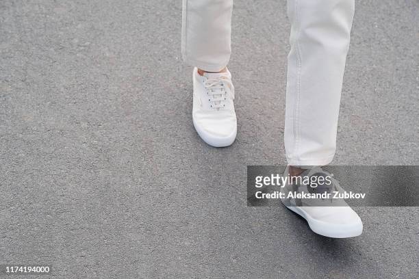 a woman in sports shoes is on the sidewalk. legs of a girl in new white sneakers and jeans. fashionable and stylish lifestyle. - white pants ストックフォトと画像