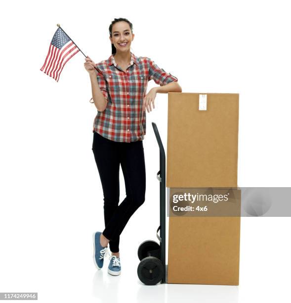 Full length / front view of 18-19 years old adult beautiful black hair / long hair / ponytail caucasian female / young women delivery person / manual worker standing in front of white background who is smiling / happy / cheerful / cool attitude