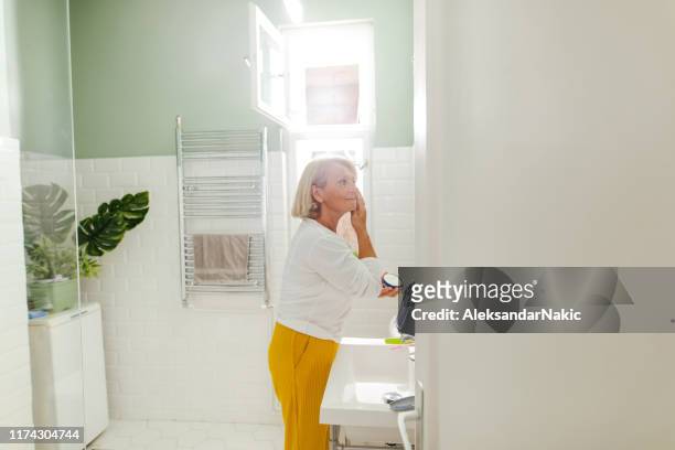 seniorin macht ihre morgenroutine im badezimmer - senioren in bad stock-fotos und bilder