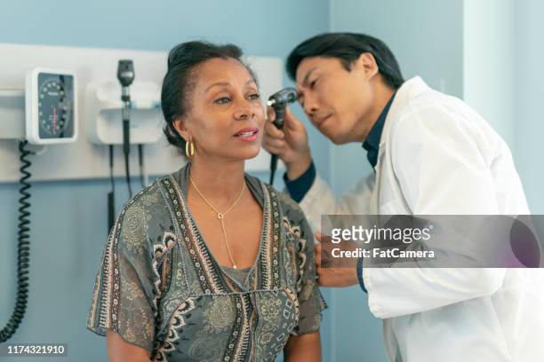 mature adult woman has ears checked by doctor at routine medical appointment - ear stock pictures, royalty-free photos & images