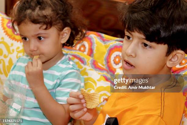 brother and sister sitting together on bed and eating potato chips - family eating potato chips imagens e fotografias de stock