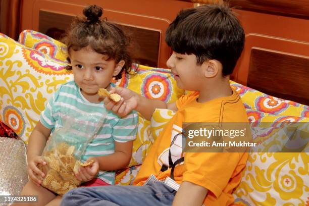 brother and sister sitting together on bed and eating potato chips - family eating potato chips imagens e fotografias de stock