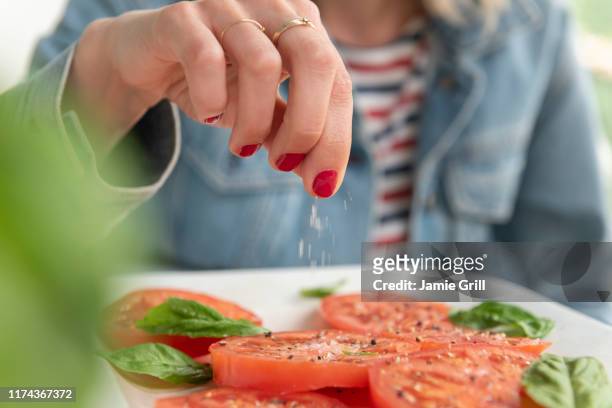 woman sprinkling salt on tomatoes - sprinkling stock pictures, royalty-free photos & images