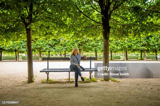 woman on park bench by trees in palais-royal gardens in paris, france - banc public photos et images de collection