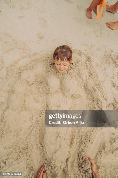 jongen begraven in zand - buried in sand stockfoto's en -beelden