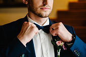 Man in a suit correcting his bow-tie. Morning preparation groom at home. Fashion photo of a man.