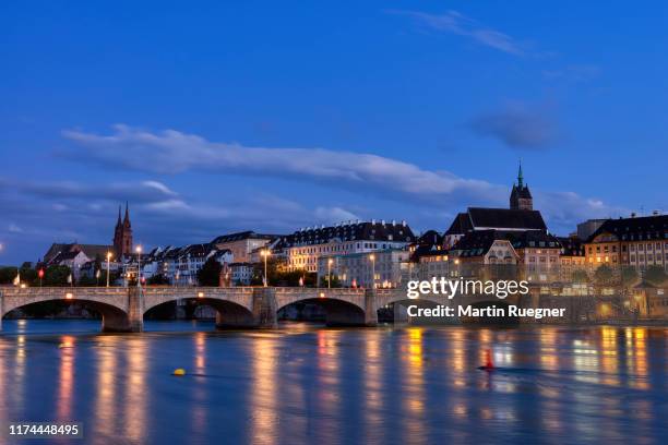 the medieval mittlere rheinbrücke (a stone brigde over river rhine) and church martinskirche with view to skyline of basel illuminated at dusk. basel, canton basel-stadt, switzerland. - bale photos et images de collection