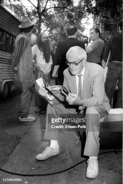 View of American psychologist and writer Timothy Leary as he sits on a sidewalk and reads an issue of People magazine , New York, 1988.