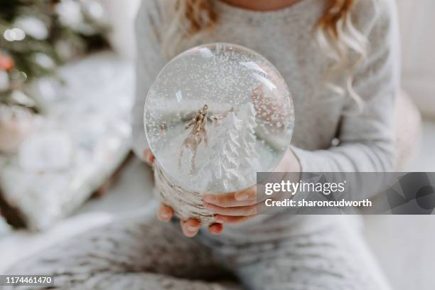 girl sitting on the floor holding a snow globe at christmas - snow globe stock-fotos und bilder