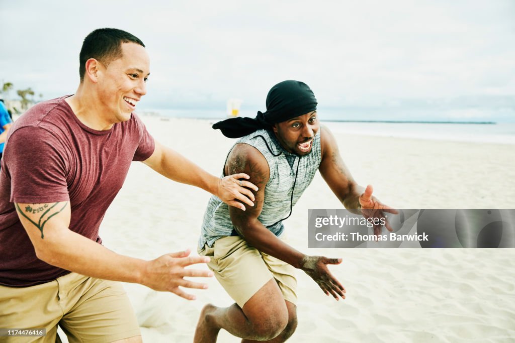 Smiling man defending opposing player going out for pass during football game on beach