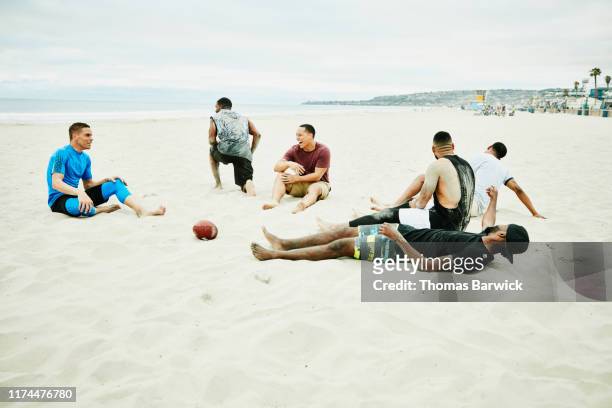laughing friends lying in sand after touchdown celebration during beach football game - hunky guy on beach stock pictures, royalty-free photos & images