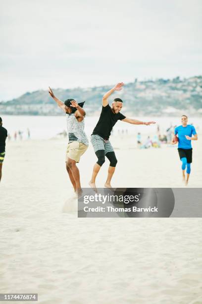 men jumping in celebration of touchdown during beach football game with friends - touchdown celebrate stock-fotos und bilder