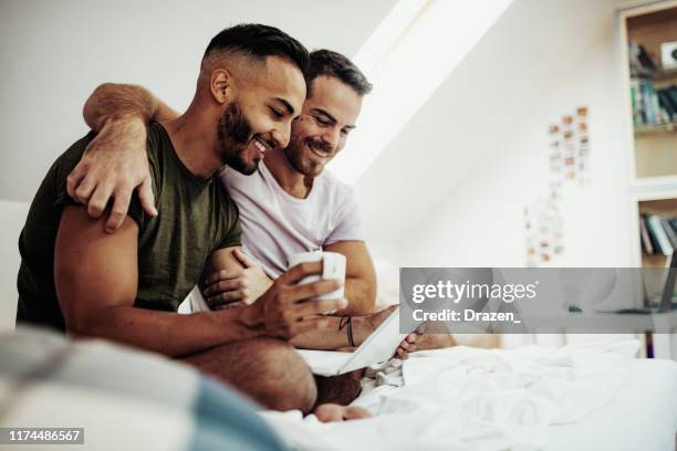 schwules paar zu hause mit internet und laptop mit freunden zu chatten - gay stock-fotos und bilder