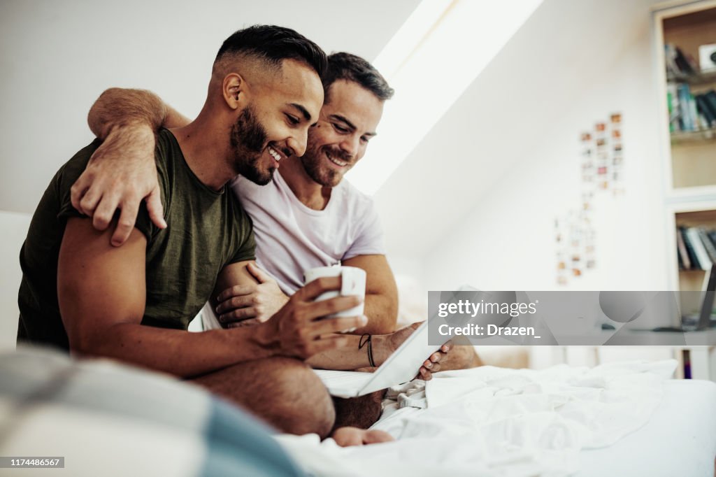 Gay couple at home using internet and laptop to chat with friends