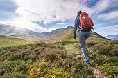 A hiker walking up a mountain ridge, The Edge, towards Ullock Pike, Carl Side and Skiddaw in the English Lake District UK.