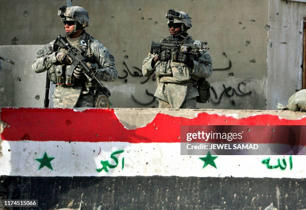 Two US soldiers from the 2nd Squadron, 2nd Stryker Cavalry Regiment walk past a concrete block with a painted-on Iraqi flag as they patrol a...