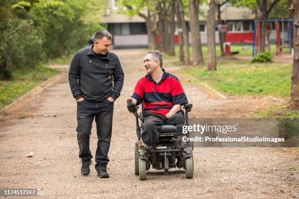 disabled person in electric wheelchair in a public park with a friend - motorized wheelchair stock pictures, royalty-free photos & images