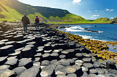 Two tourists walking at Giants Causeway, an area of hexagonal basalt stones, County Antrim, Northern Ireland. Famous tourist attraction, UNESCO World Heritage Site.