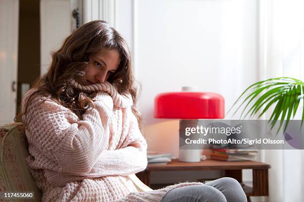young woman wearing sweater sitting with arms folded, looking down in thought - cold woman stock-fotos und bilder