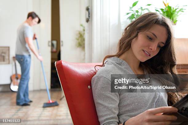 woman reading magazine while her husband sweeps the floor - husband cleaning stock pictures, royalty-free photos & images