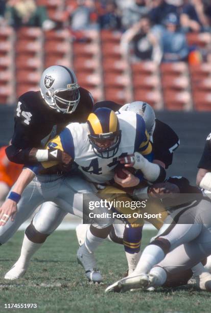 Mike Guman of the Los Angeles Rams gets tackled by Howie Long and Burgess Owens of the Los Angeles Raiders during an NFL football game December 18,...