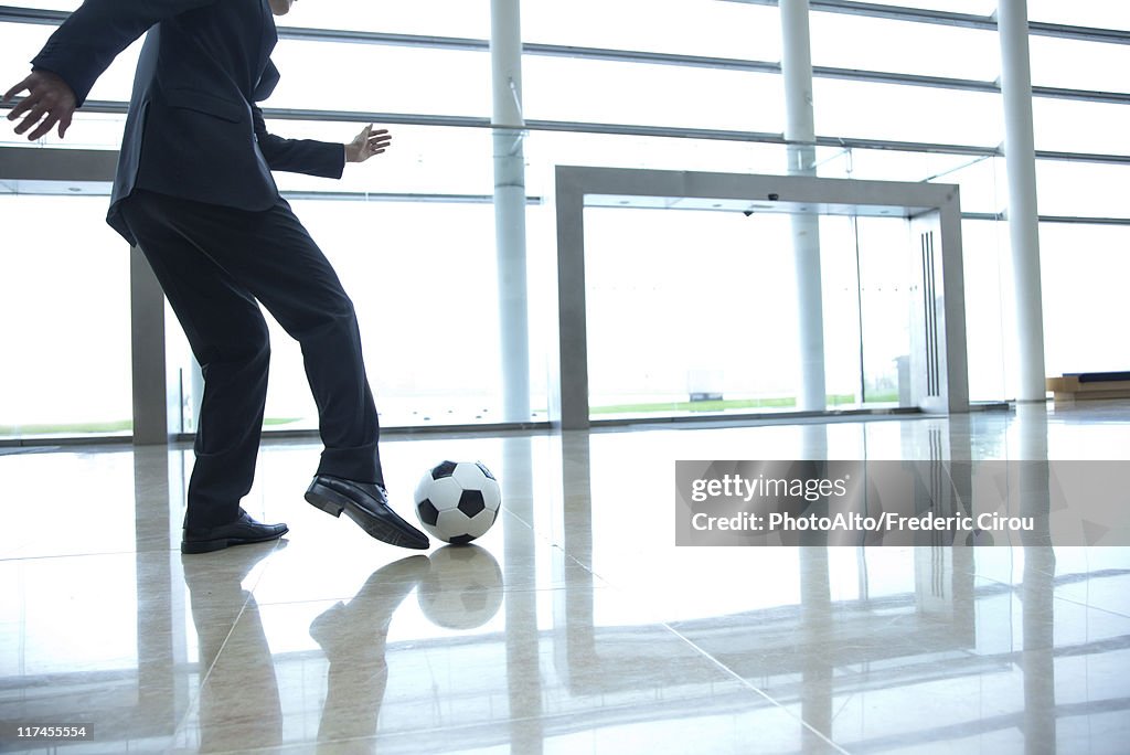 Businessman kicking soccer ball in lobby