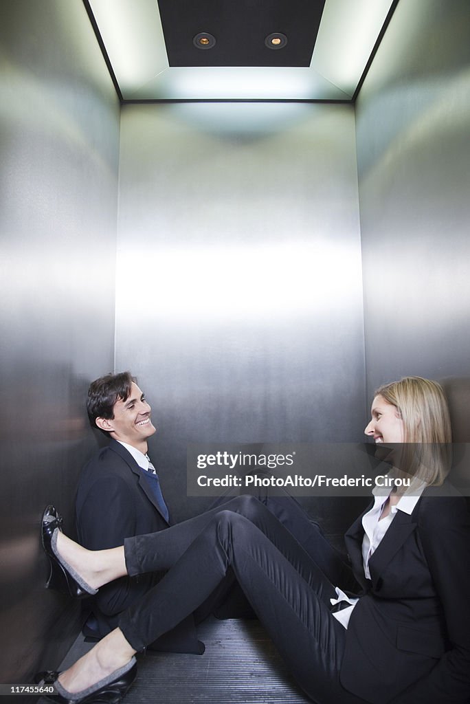 Professionals trapped in elevator, sitting on floor chatting