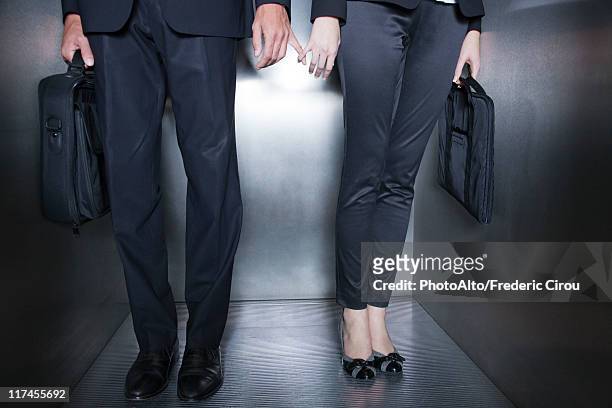 colleagues holding hands in elevator, low section - business couple stockfoto's en -beelden