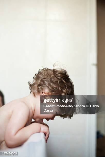 toddler boy leaning over side of bathtub crying - trotzanfall stock-fotos und bilder