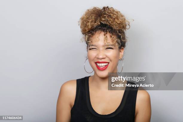 portrait of young latinx woman with curly blonde hair in a bun, wearing red lipstick and a black tank top, in front of a grey background. - chignon bun photos et images de collection