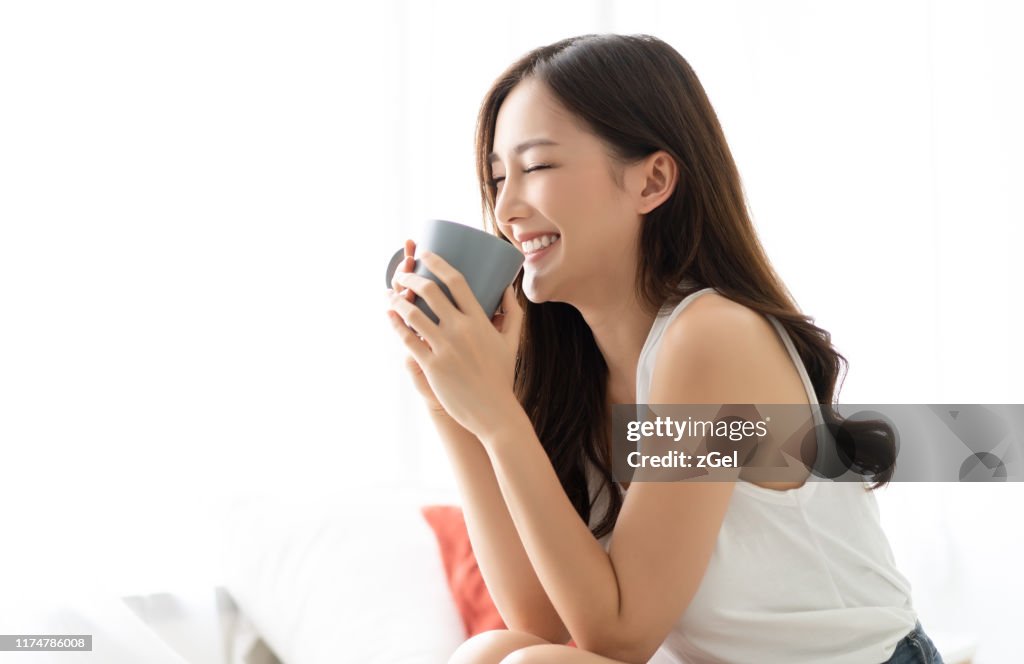 Happy smiling beautiful Asian woman awaking with cup of coffee at bedroom with Eyes Closed. People Lifestyle concept;