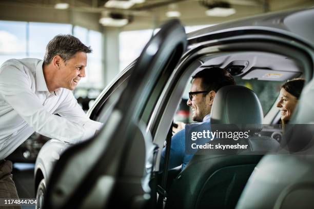 happy car salesperson talking to young couple in a showroom. - car salesman stock pictures, royalty-free photos & images