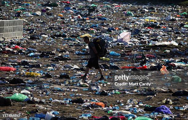 Festival goers walk through rubbish left in the main arena in front of the Pyramid Stage as they begin to leave the Glastonbury Festival site on June...