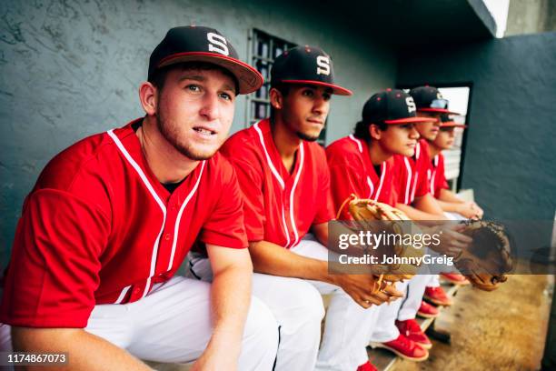 baseball players sitting on dugout bench and watching game - sideline baseball stock pictures, royalty-free photos & images